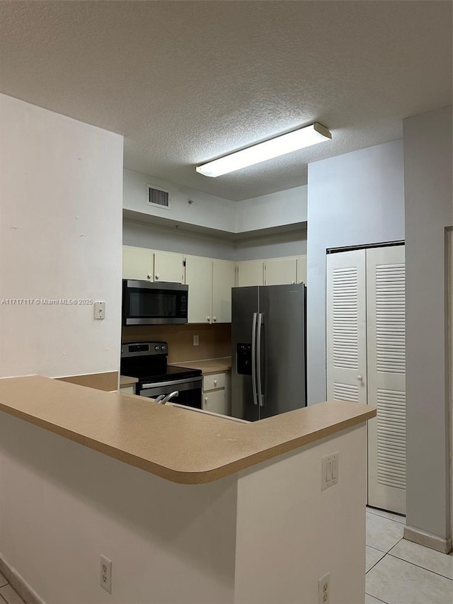 kitchen with light tile patterned flooring, kitchen peninsula, a textured ceiling, and appliances with stainless steel finishes