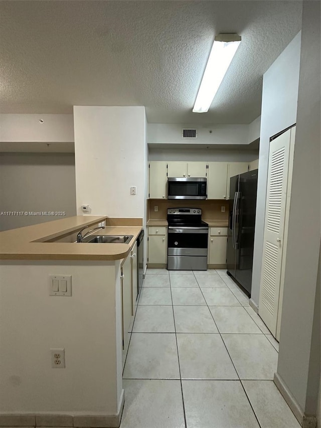 kitchen with kitchen peninsula, light tile patterned floors, a textured ceiling, and stainless steel appliances