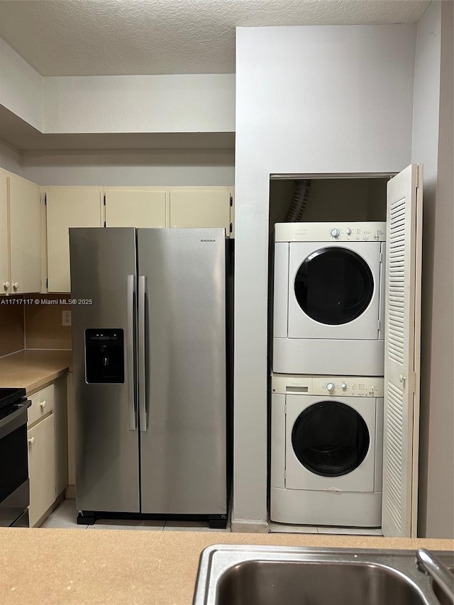 kitchen with cream cabinetry, a textured ceiling, appliances with stainless steel finishes, and stacked washer and clothes dryer