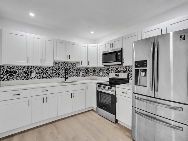 kitchen featuring white cabinetry, sink, tasteful backsplash, appliances with stainless steel finishes, and light wood-type flooring