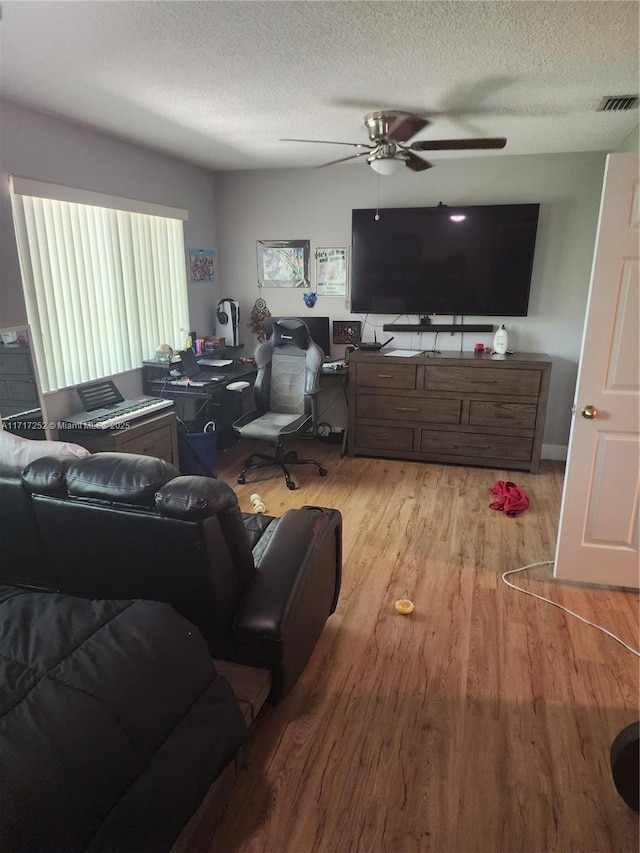 living room featuring ceiling fan, light wood-type flooring, and a textured ceiling