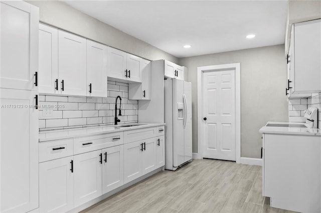 kitchen with light wood-type flooring, light stone counters, sink, white refrigerator with ice dispenser, and white cabinetry