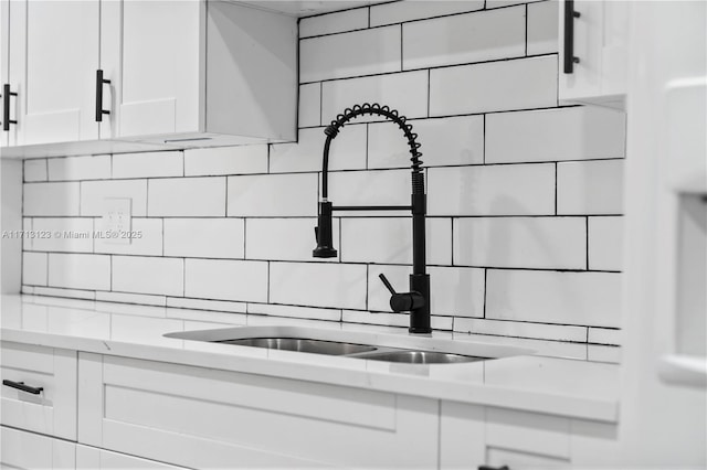 interior space with decorative backsplash, sink, white cabinets, and light stone counters