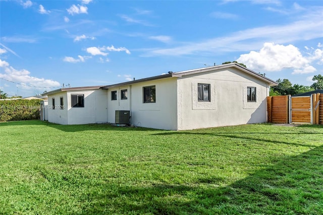 rear view of house with central air condition unit and a lawn