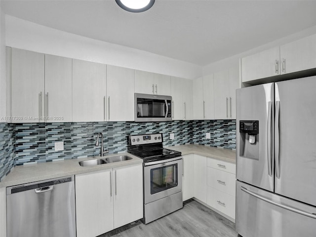 kitchen featuring light hardwood / wood-style flooring, backsplash, white cabinetry, appliances with stainless steel finishes, and sink