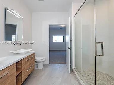 full bath with marble finish floor, vanity, a shower stall, and toilet