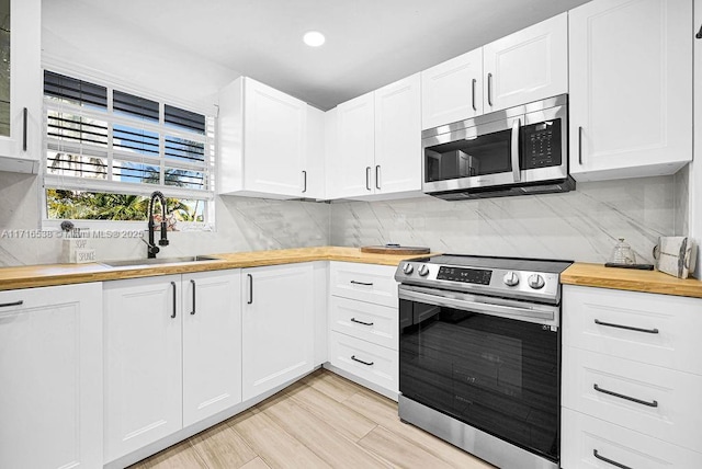 kitchen featuring sink, stainless steel appliances, wood counters, decorative backsplash, and white cabinets