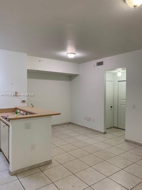 kitchen with kitchen peninsula, a textured ceiling, and light tile patterned flooring