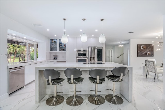 kitchen featuring appliances with stainless steel finishes, a kitchen breakfast bar, white cabinets, hanging light fixtures, and a large island