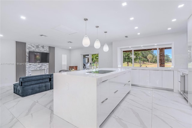 kitchen with a large fireplace, hanging light fixtures, black electric stovetop, a center island with sink, and white cabinets