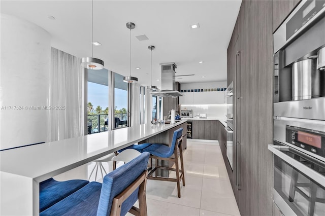 kitchen with white cabinets, hanging light fixtures, a breakfast bar area, light tile patterned flooring, and island exhaust hood