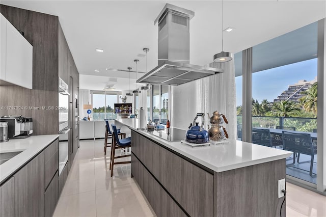 kitchen with island exhaust hood, black cooktop, light tile patterned floors, decorative light fixtures, and a large island