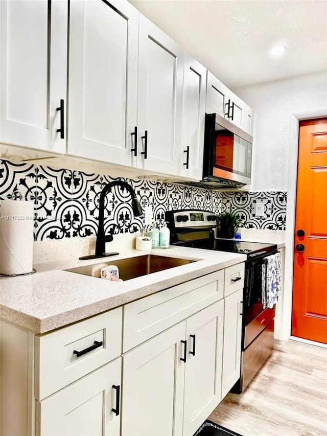 kitchen featuring backsplash, light stone counters, sink, electric range, and white cabinets