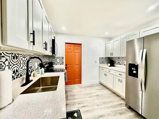 kitchen featuring sink, light stone counters, stainless steel fridge, decorative backsplash, and white cabinets