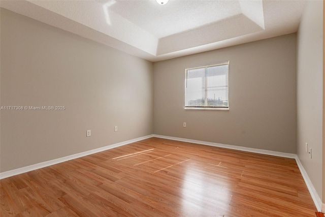 unfurnished room with a tray ceiling, a textured ceiling, and light wood-type flooring