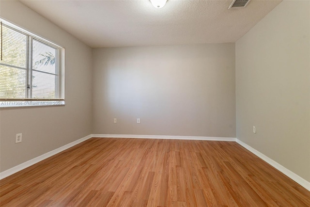 spare room with light wood-type flooring and a textured ceiling