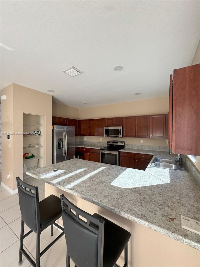 kitchen with light tile patterned flooring, a kitchen bar, kitchen peninsula, and appliances with stainless steel finishes