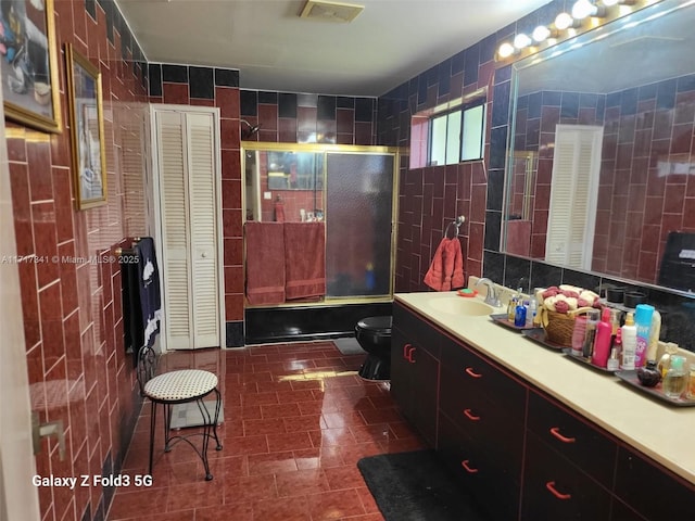 full bathroom with combined bath / shower with glass door, tile walls, vanity, tasteful backsplash, and toilet