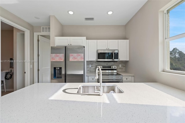 kitchen featuring appliances with stainless steel finishes, a wealth of natural light, white cabinetry, sink, and light stone counters