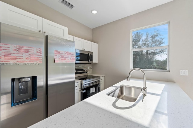 kitchen with white cabinetry, stainless steel appliances, sink, and light stone counters