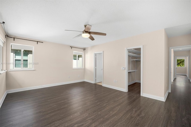 unfurnished bedroom with a walk in closet, a textured ceiling, ceiling fan, dark wood-type flooring, and a closet