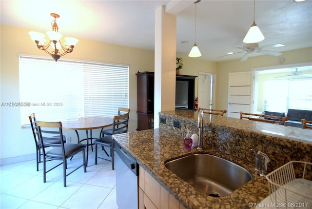 kitchen with dishwasher, dark stone counters, decorative light fixtures, light tile patterned floors, and ceiling fan with notable chandelier