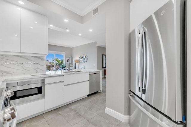 kitchen with sink, white cabinets, backsplash, ornamental molding, and stainless steel appliances