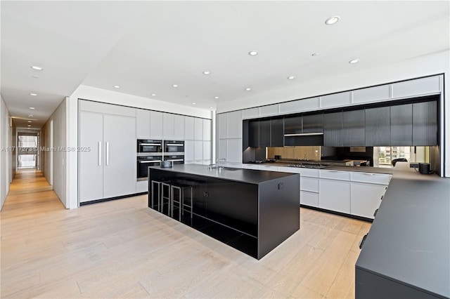 kitchen featuring sink, double oven, a large island, light hardwood / wood-style floors, and white cabinetry