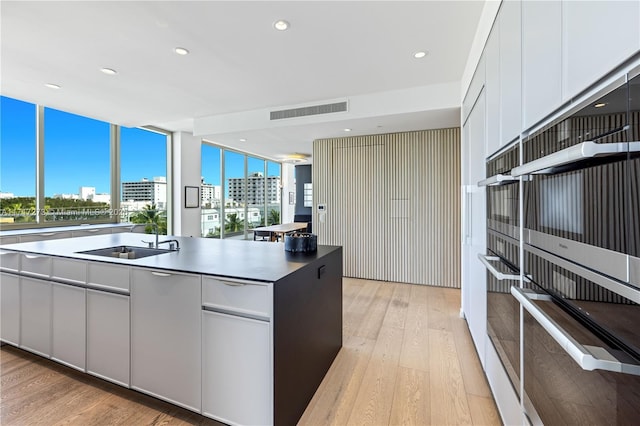 kitchen featuring white cabinets, light hardwood / wood-style flooring, expansive windows, and sink