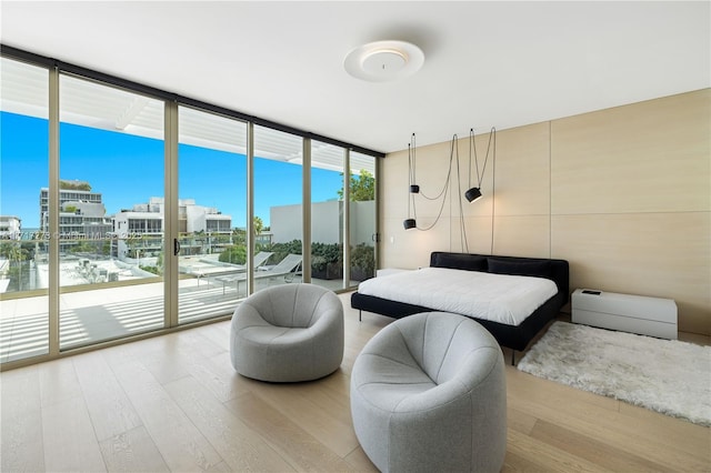 bedroom featuring access to exterior, light wood-type flooring, a water view, and floor to ceiling windows