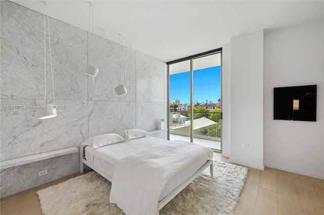 bedroom with access to exterior, light hardwood / wood-style flooring, floor to ceiling windows, and tile walls