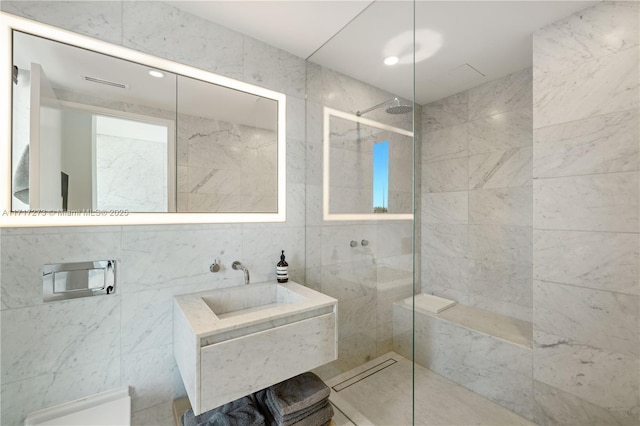 bathroom featuring tiled shower, vanity, and tile walls