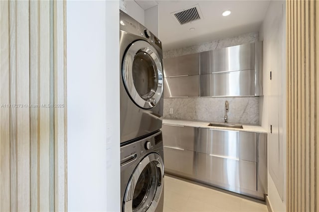 clothes washing area featuring light tile patterned floors, stacked washer and dryer, and sink