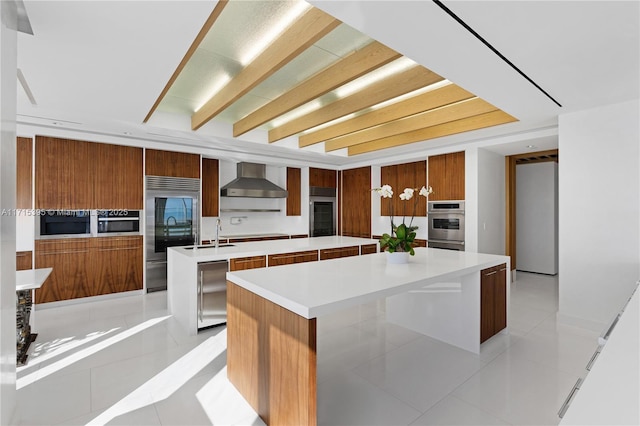 kitchen featuring light tile patterned floors, a spacious island, wall chimney range hood, and appliances with stainless steel finishes