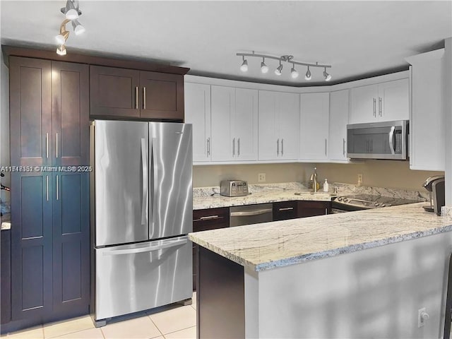 kitchen with sink, light tile patterned floors, light stone counters, white cabinetry, and stainless steel appliances