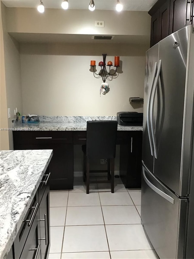 kitchen featuring an inviting chandelier, light stone countertops, light tile patterned flooring, dark brown cabinetry, and stainless steel refrigerator