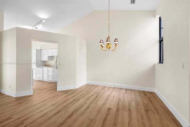 spare room featuring a chandelier, light wood-type flooring, rail lighting, and vaulted ceiling