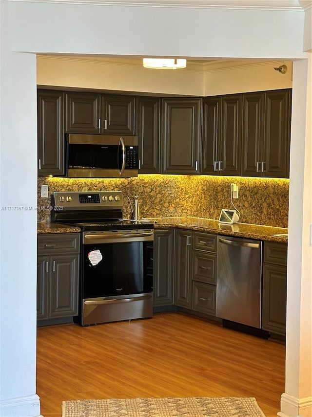 kitchen with light wood finished floors, appliances with stainless steel finishes, dark stone countertops, and decorative backsplash