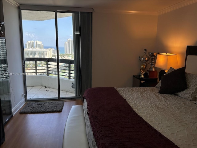 bedroom featuring access to exterior, a view of city, crown molding, and wood finished floors