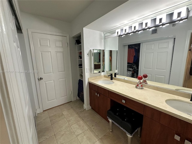 bathroom with a walk in closet, visible vents, a sink, and double vanity