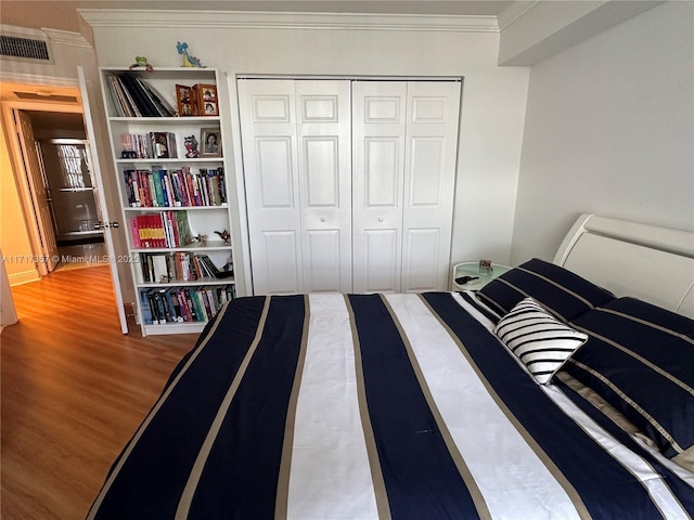 bedroom featuring ornamental molding, a closet, wood finished floors, and visible vents