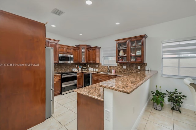 kitchen featuring sink, appliances with stainless steel finishes, backsplash, light stone countertops, and kitchen peninsula