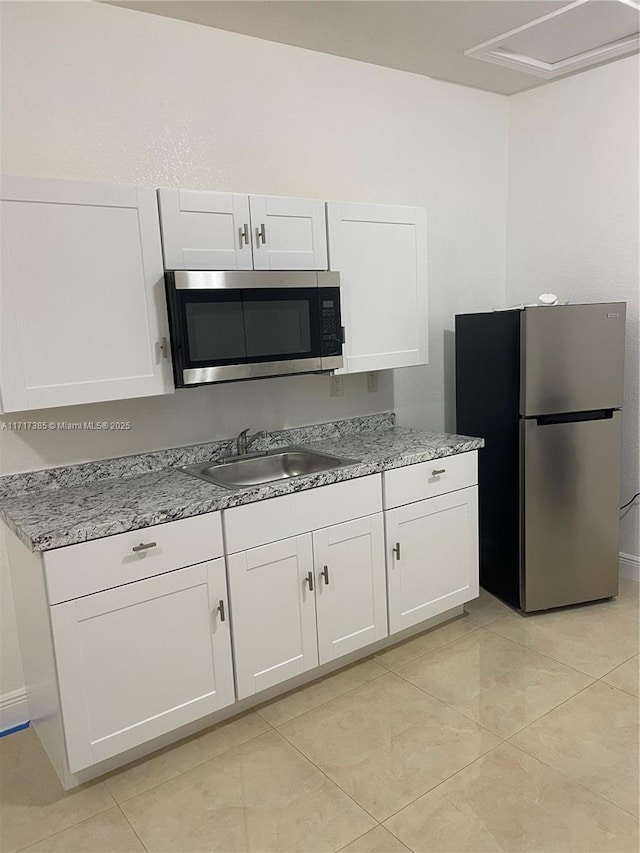 kitchen featuring stainless steel appliances, white cabinetry, light stone countertops, and sink