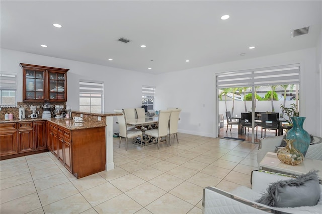 kitchen featuring light tile patterned floors, decorative backsplash, light stone countertops, and kitchen peninsula