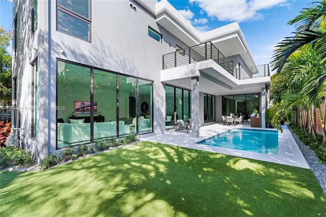 rear view of property with a balcony, a fenced in pool, a patio area, and a lawn