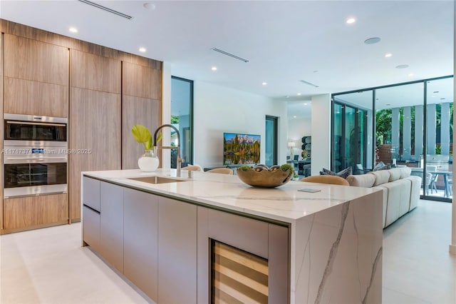 kitchen with light stone countertops, floor to ceiling windows, stainless steel double oven, sink, and a large island