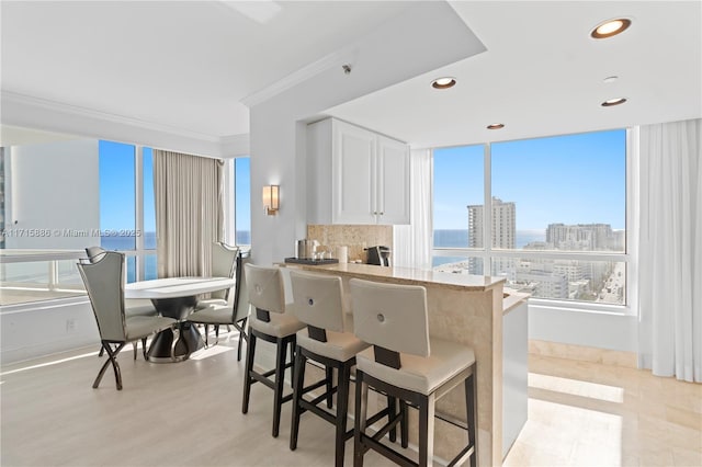 kitchen with a water view, kitchen peninsula, ornamental molding, white cabinetry, and a breakfast bar area