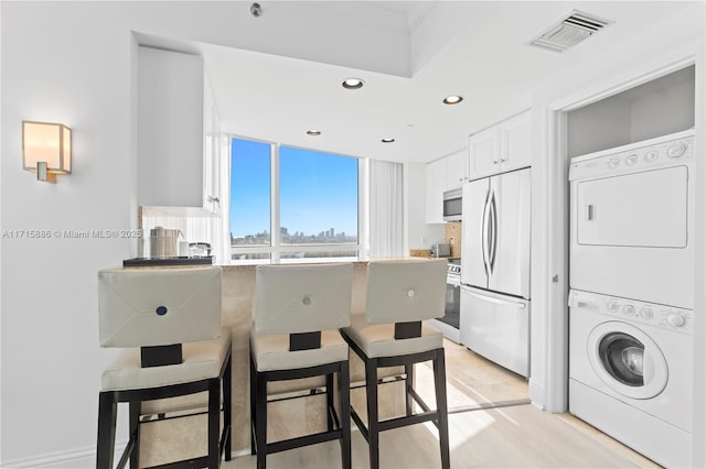 kitchen featuring stacked washer / drying machine, light wood-type flooring, white cabinetry, and appliances with stainless steel finishes