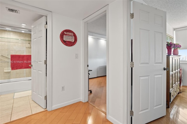 hall with light hardwood / wood-style floors and a textured ceiling