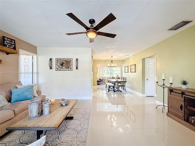 living room featuring ceiling fan with notable chandelier, light tile patterned floors, and a textured ceiling